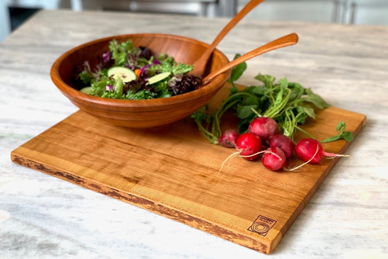 wood salad bowl with wood salad servers and wood cutting board shown in cherry