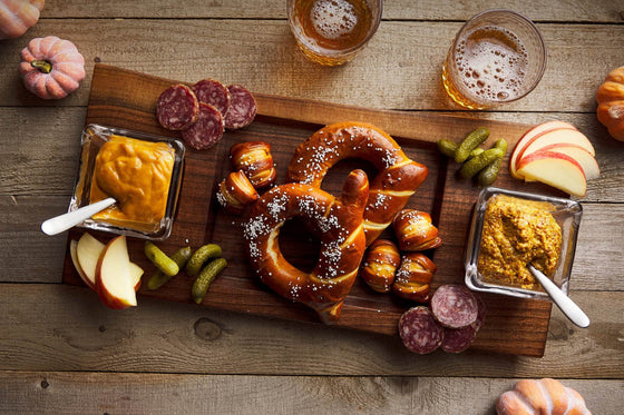 Wood cutting board shown with pretzels charcuterie and beer