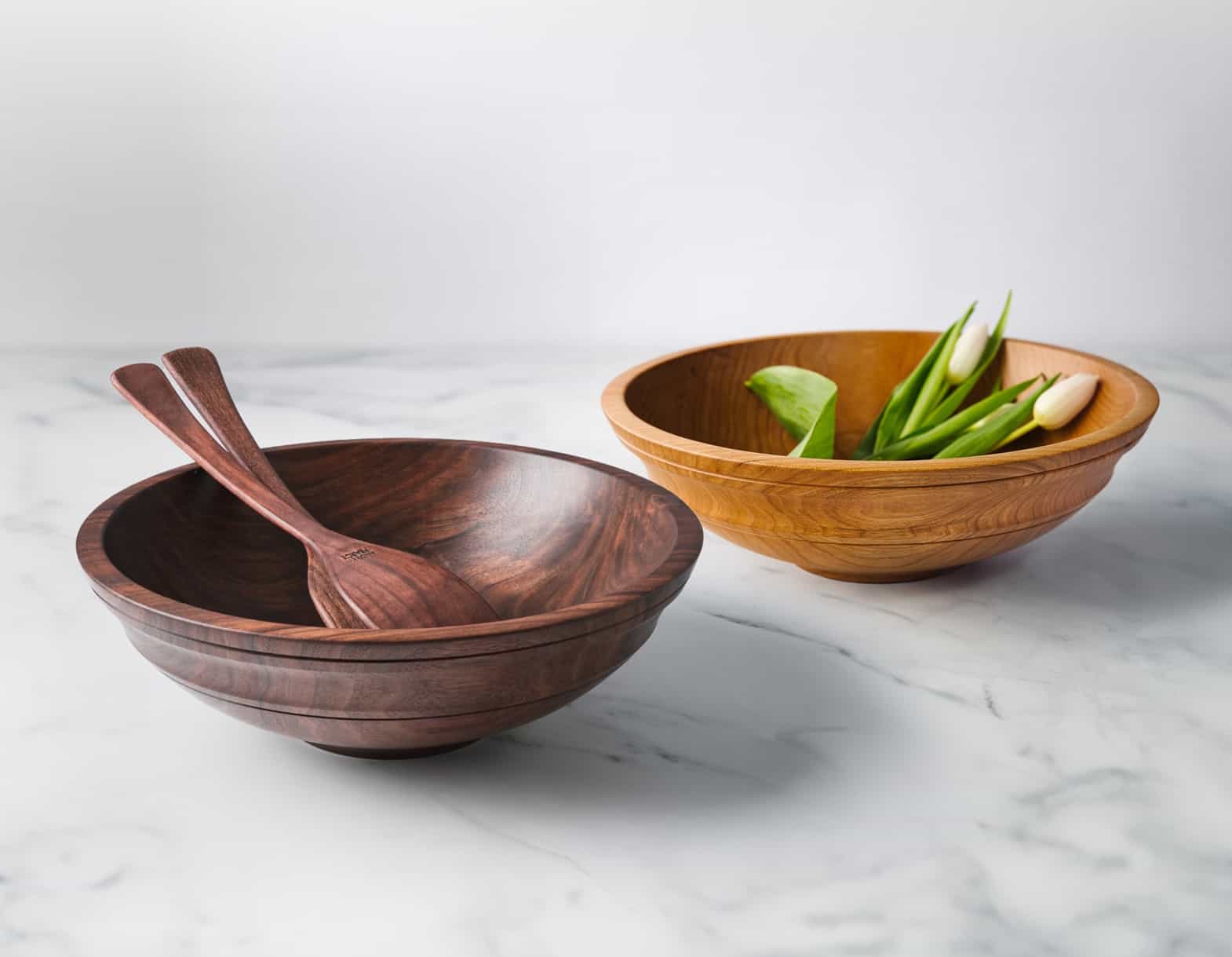 wooden bowls and wood salad bowls from Andrew Pearce Bowls shown with wooden salad servers and fresh cut flowers. One wooden bowls is in walnut and the other bowl is in cherry.